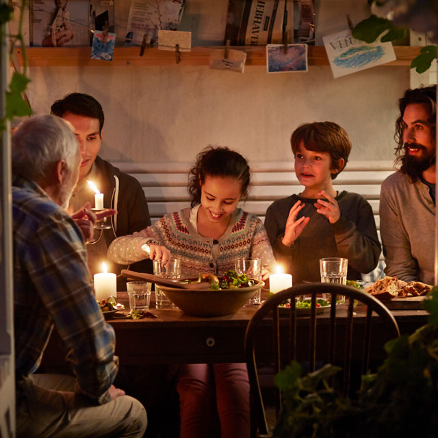Two men, two boys and a girl sit at a candlelit dining table.