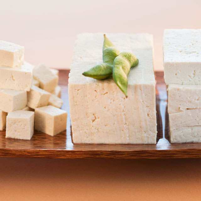 Closeup photo of a a block of tofu on a wooden platter.