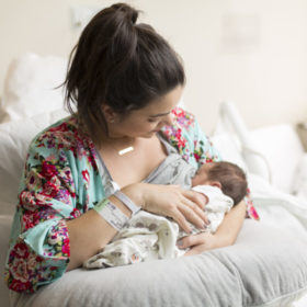A young mother breastfeeds a newborn in bed.