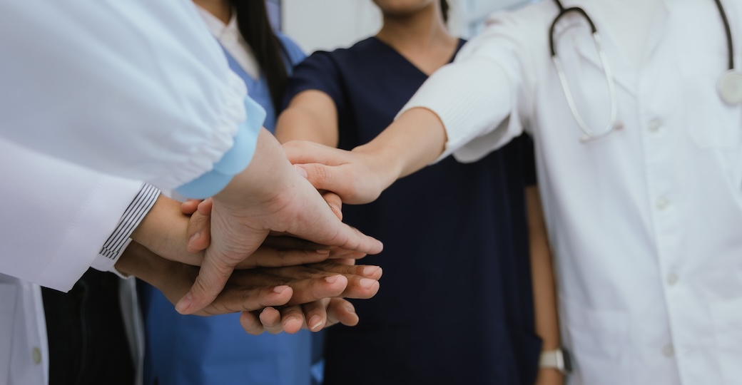 Four medical professionals put their hands together to show collaboration.
