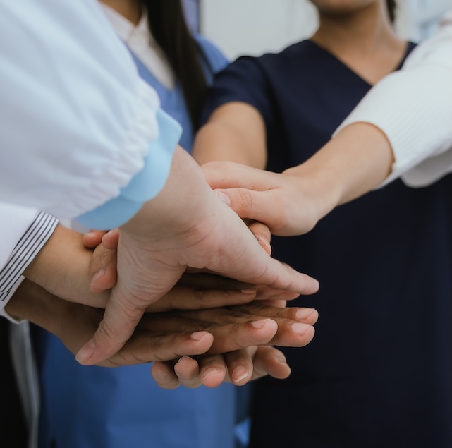 Four medical professionals put their hands together to show collaboration.