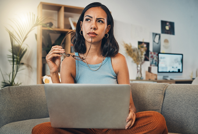 Thinking woman sitting with laptop and glasses in her hands