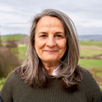 Head-and-shoulders portrait of a middle aged white woman standing outdoors.