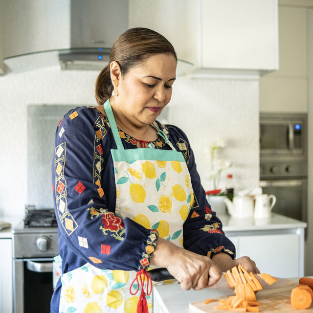 A Latina woman chops vegetables in a home kitchen.