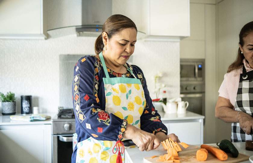 A Latina woman chops vegetables in a home kitchen.