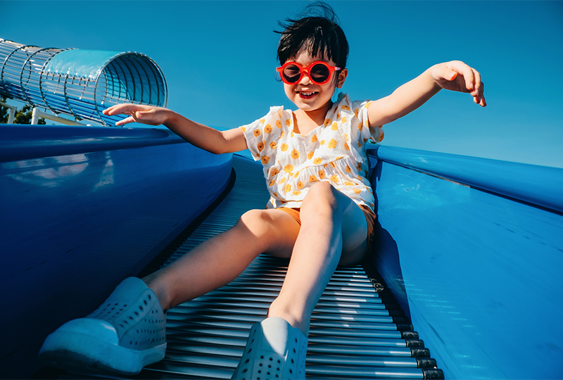Asian child in sunglasses on slide with feet in foreground