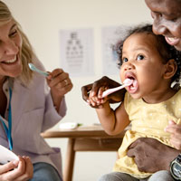 A toddler gets help from her dad and a dentist with brushing her teeth.