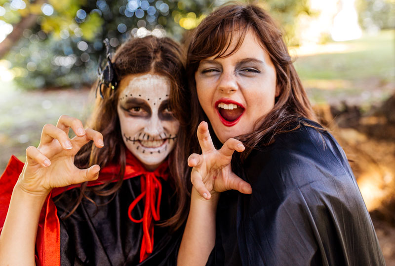 Two preteen girls make faces at the camera wearing Halloween witch costumes and face paint.