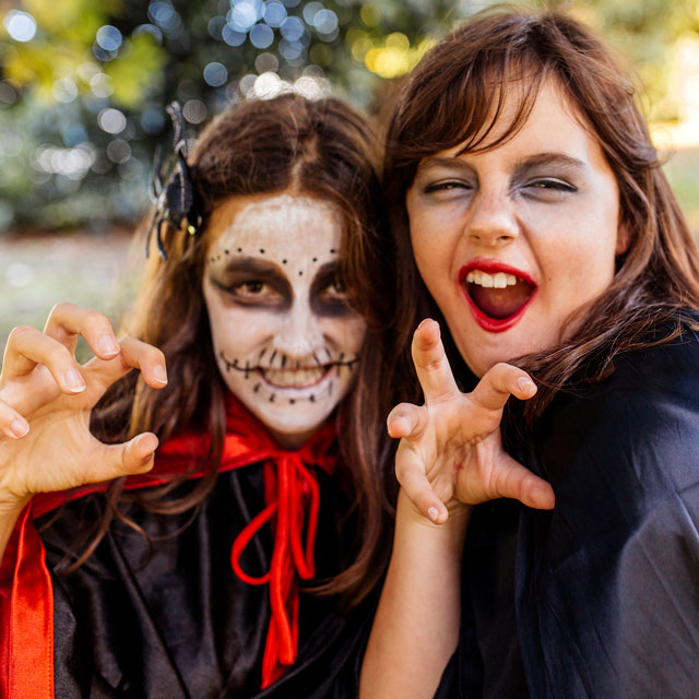 Two preteen girls make faces at the camera wearing Halloween witch costumes and face paint.