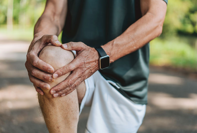 Closeup of a man standing and holding his right knee up in a stretch.