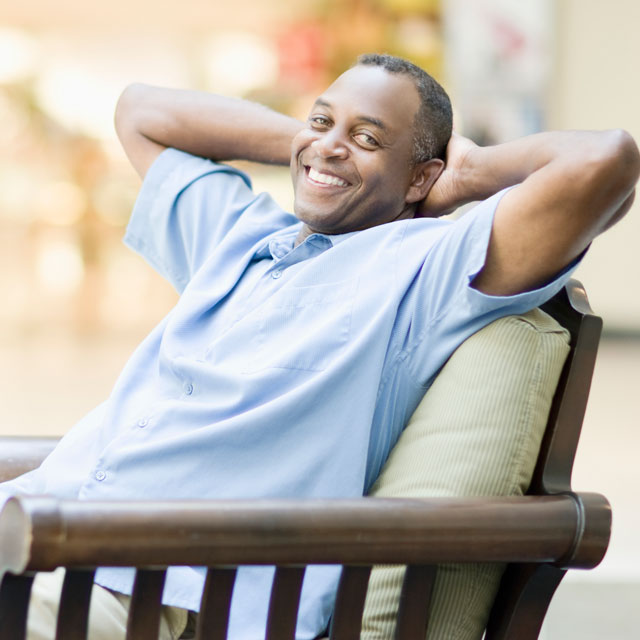A man in his early 40s relaxing on a patio bench.