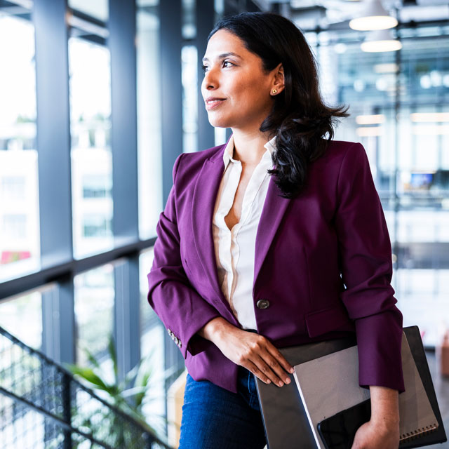 A woman who looks to be in her late 30s pauses on a stair landing to look out a window.