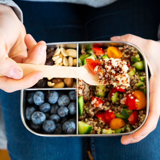 Overhead close-up view of a bento box meal of quinoa veggie salad, blueberries and nuts.