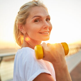 A young white woman holds a light dumbbell.