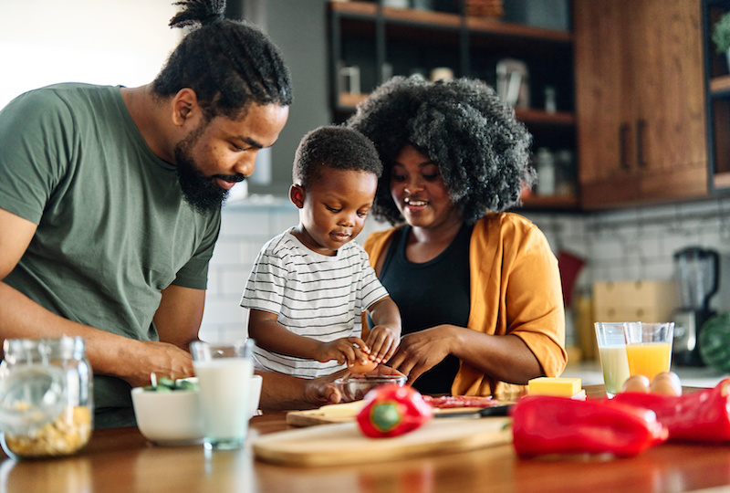 Parents chop red peppers with their toddler in the kitchen.