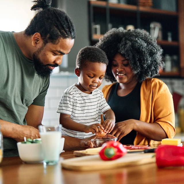 Parents chop red peppers with their toddler in the kitchen.