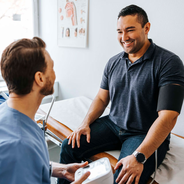 A male nurse checks a middle-aged male patient's blood pressure in a medical office.