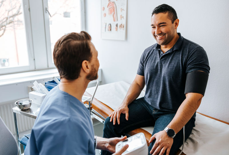 A male nurse checks a middle-aged male patient's blood pressure in a medical office.