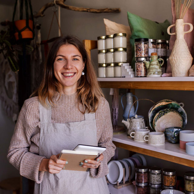 A woman stands by open shelves of plates and bowls as in a cafe.
